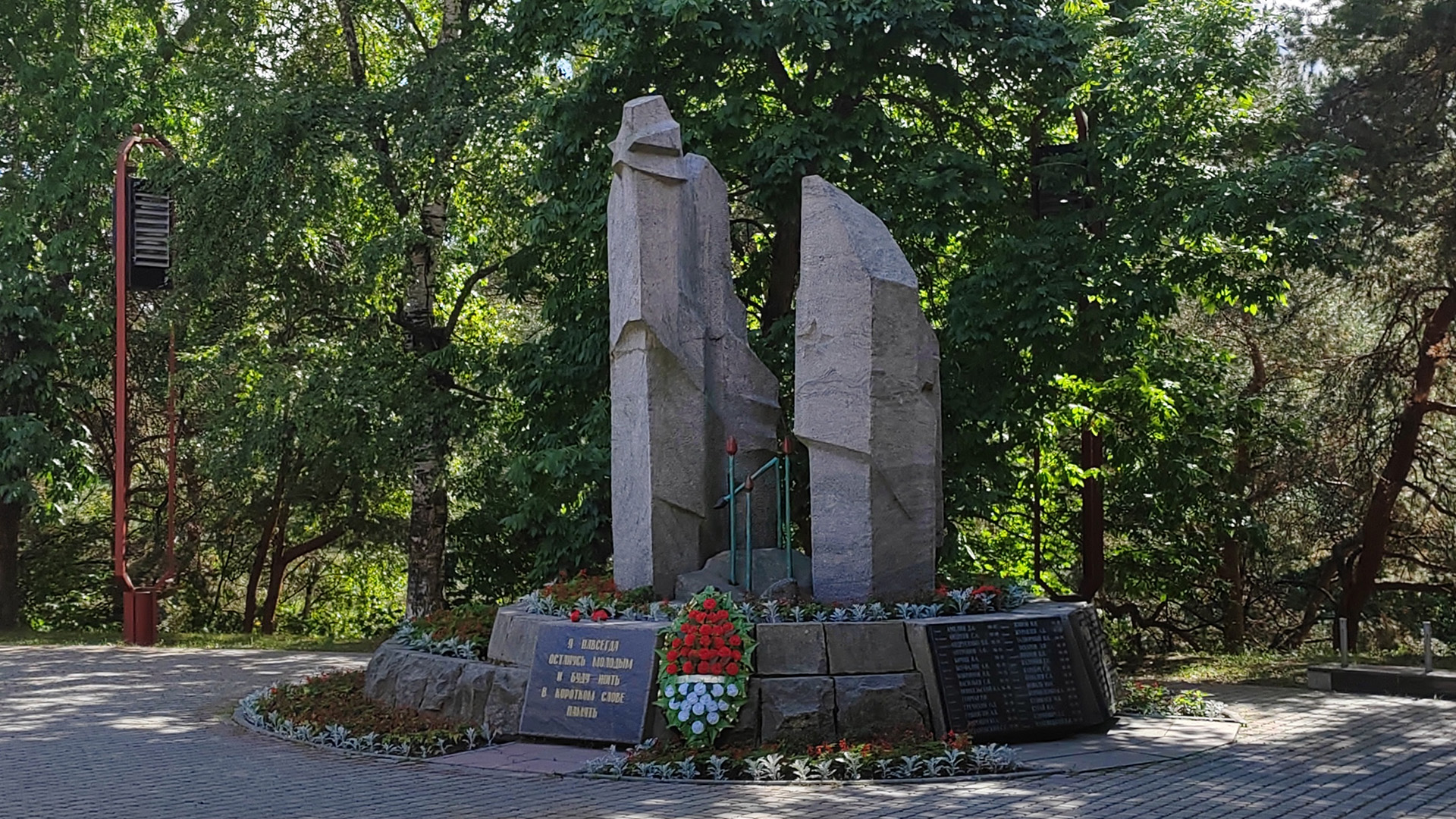 Мемориал «Чёрный тюльпан» Мемориал в виде трёх гранитных камней тёмно-серого цвета, обрамлённых оградой на фоне деревьев.