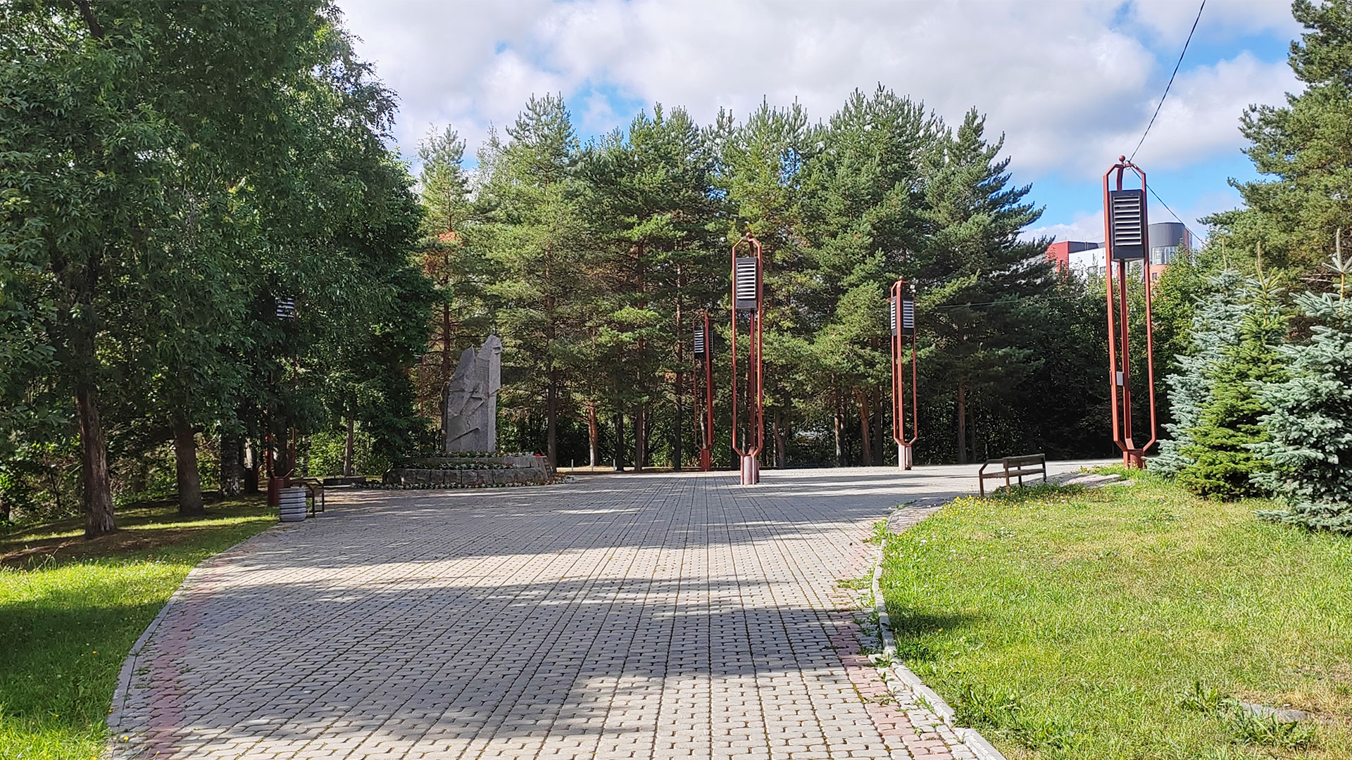 Мощёная аллея ведущая к монументу в обрамлении хвойных и лиственных деревьев.