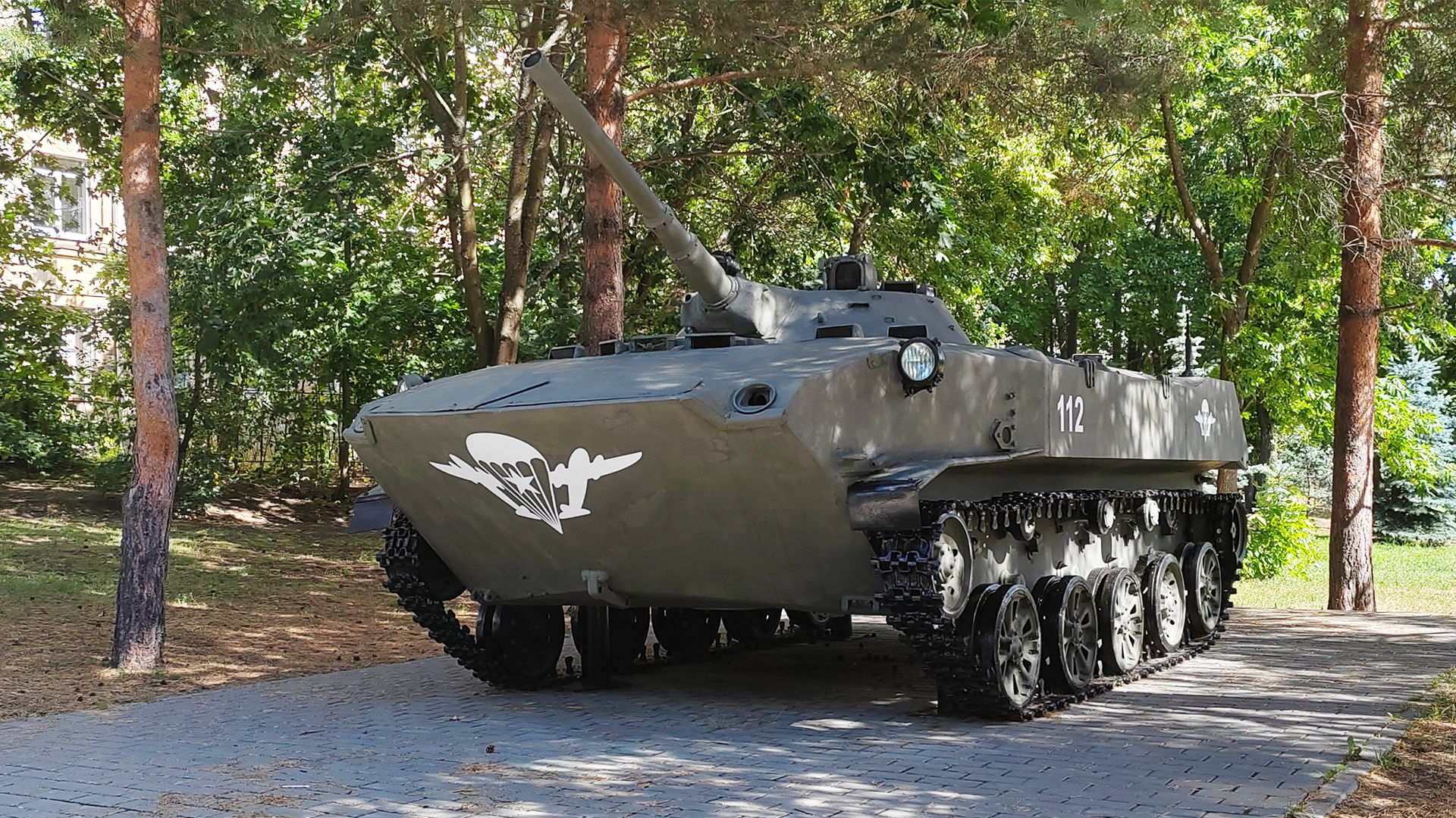 Боевая машина десанта БМД-1 Боевая машина на гусеничном ходу, вооружённая пушкой установленная на мощёной площадке среди деревьев.