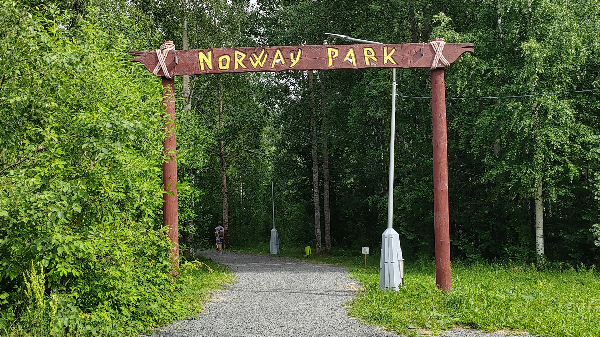 Деревянная арка с надписью «Norway Park» над грунтовой аллеей ведущей в лесной массив.