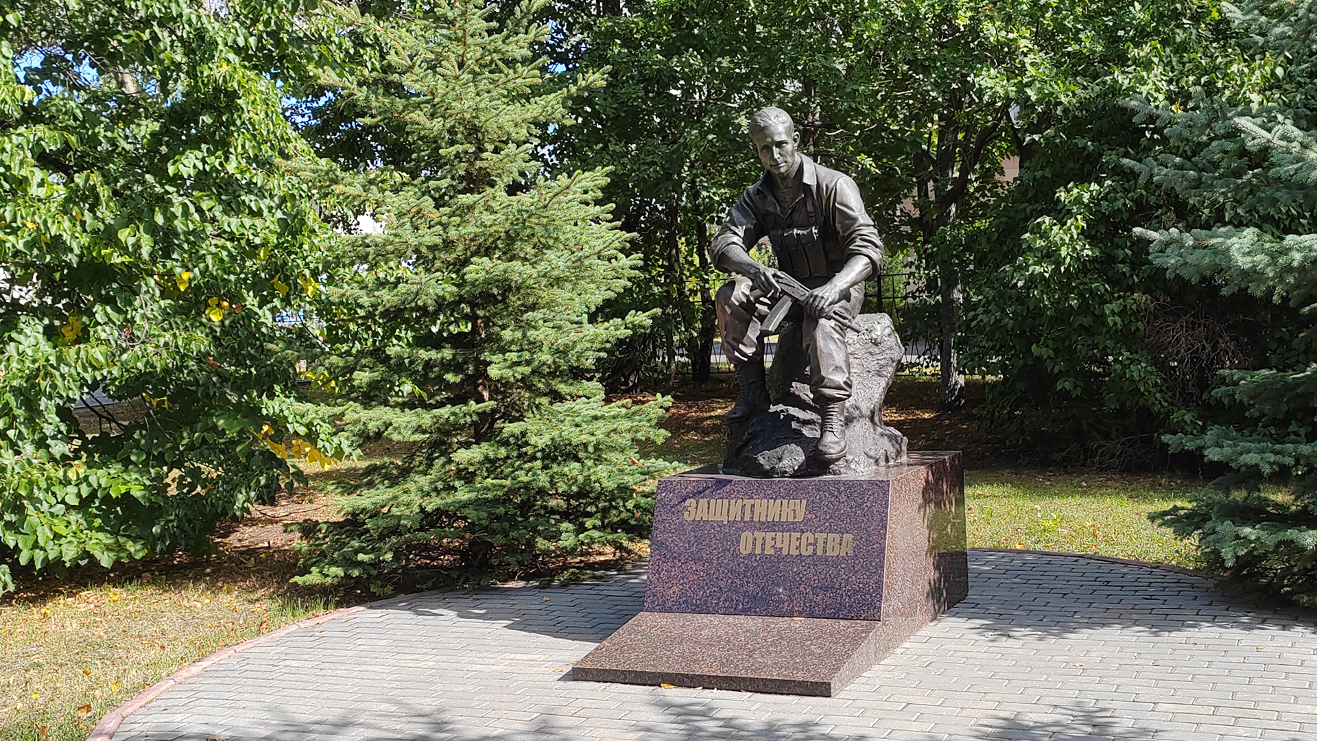 Монумент «Защитнику Отечества» Фигура солдата сидящего на камне с автоматом в руках на каменном постаменте с надписью.
